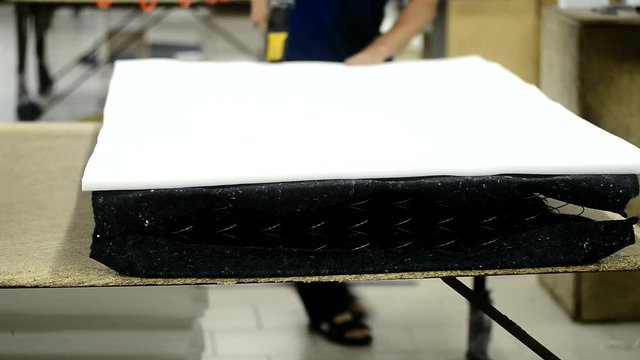Worker puts foam rubber on spring base and fasten in mattress factory