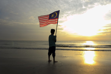 The Concept of Independence Day - a boy holding the Malaysian flag on the shore at sunrise