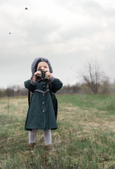 Child in vintage coat watching birds through old binoculars on a cloudy day.