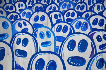 The old wall, painted in color graffiti drawing with aerosol paints. The image of a set of identical cartoon faces. The concept of a mindless crowd