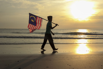 The Concept of Independence Day - a boy holding the Malaysian flag on the shore at sunrise