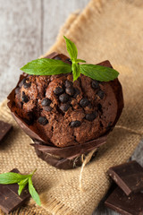 chocolate dark muffin with a leaf of mint on a wooden table with cinnamon, anise, chocolate