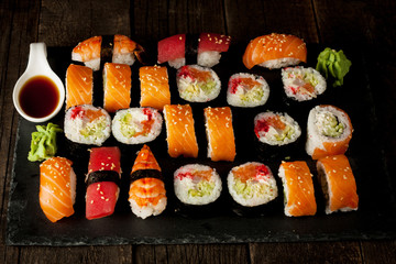Sashimi and sushi rolls on a stone slatter. Sushi set with salmon, prawns, soy souce, wasabi and ginger. Traditional Japanese cuisine.