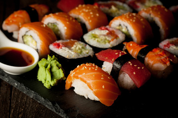 Sashimi and sushi rolls on a stone slatter. Sushi set with salmon, prawns, soy souce, wasabi and ginger. Traditional Japanese cuisine.