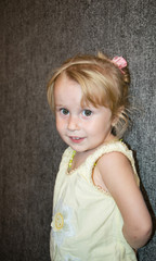 Blonde smiling little girl in a yellow dress posing in studio on a dark background.