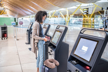 happy black woman using the check-in machine at the airport getting the boarding pass.