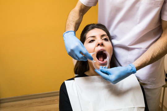Unrecognizable dentist applying mouth expander to client for examine in cabinet.