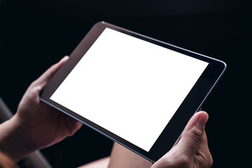 Mockup image of a woman's hands holding black tablet pc with blank white screen on thigh in black background