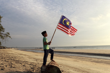 The Concept of Independence Day - a boy holding the Malaysian flag on the shore