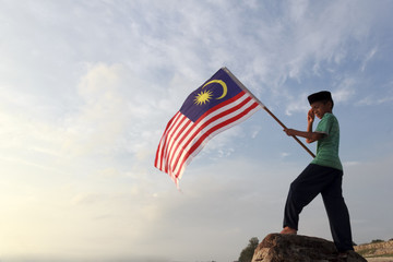The Concept of Independence Day - a boy holding the Malaysian flag on the shore