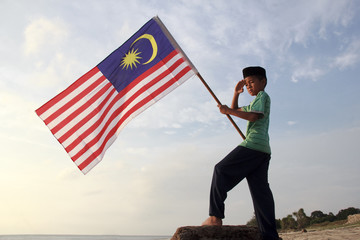 The Concept of Independence Day - a boy holding the Malaysian flag on the shore