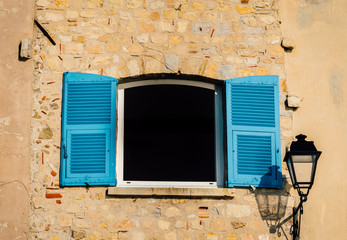 Bright blue shutters with a lamp post on a rustic wall in Provence, France