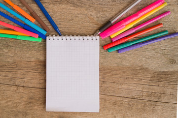 Open white notepad with colorful felt-tip pens and ball pens on the wooden table