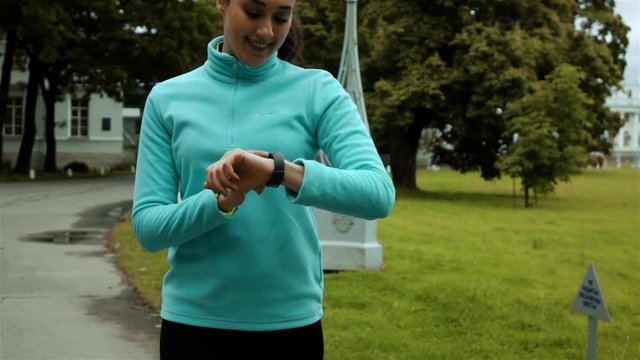 Runner using smart watch fitness tracker and heart rate monitor. Middle steadicam slow motion shot. Female athlete checking her cardio training data during workout outside in running park.