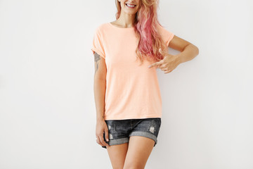 Cropped shot of stylish smiling woman wearing loose T-shirt and jean shorts, pointing at copy space for your text or advertising content. Female with slim body advertising while trying new clothes