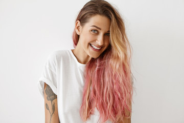 Style, fashion and hair coloring concept. Portrait of gorgeous young female with charming smile, tattoo on arm and long loose hair dyed pink looking at camera, having joyful carefree expression