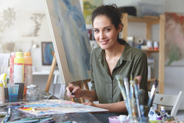 Portrait of young talented female artist making sketches with brightful oils, drawing on easel,...