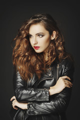 Beautiful young woman posing in black leather jacket over grey background. Fashion concept.