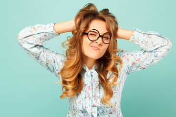 Portrait of a beautiful young student wearing glasses and showing funny emotions on face over blue background
