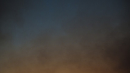 Fototapeta na wymiar Cielo in fiamme durante il tramonto. Nel cielo si espandono nuvole grigie di fumo provenienti dalle fiamme che divampano sulla terra e che danno quel colore arancione in basso.