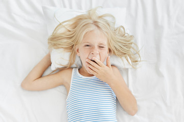 Sleepy girl waking up early in morning, covering mouth with hand while yawning, going to school or...