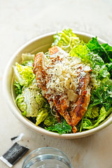 Chicken Ceasar salad. Cos lettuce leaves, grilled chicken breast sliced, parmesan cheese. Restaurant table.
