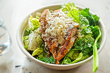Chicken Ceasar salad. Cos lettuce leaves, grilled chicken breast sliced, parmesan cheese. Restaurant table.