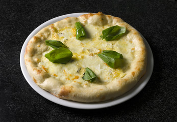 pizza quattro formaggi on a white plate on a black marble