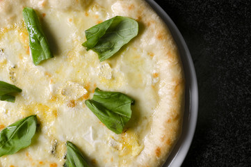 pizza quattro formaggi on a white plate on a black marble