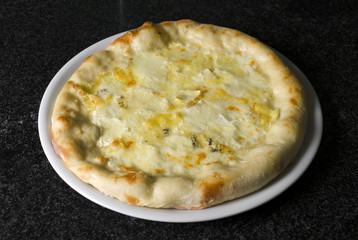 pizza quattro formaggi on a white plate on a black marble