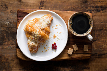 Almond croissant and cup of black coffee espresso on wooden cutting board. Table top view