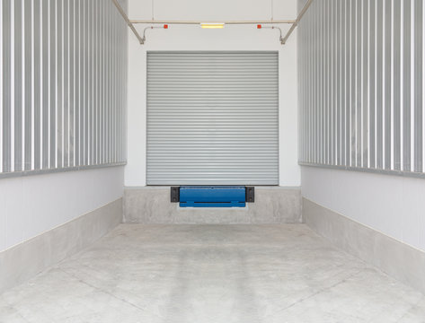 Roller door or roller shutter and dock leveler or height adjustable platform outside warehouse. Use as bridge between dock and truck for loading, storage, warehousing, shipping and freight forwarding.