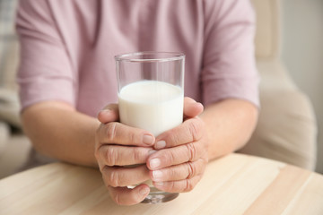 Old woman holding glass with fresh milk at table, closeup