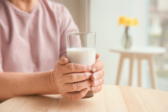 Old woman holding glass with fresh milk at table, closeup