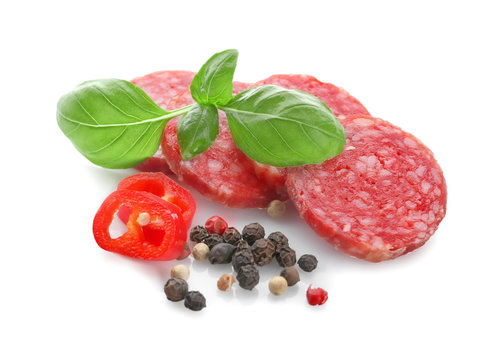 Delicious sliced sausage with chili pepper and basil on white background