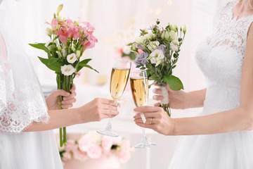 Young brides holding bouquets of beautiful flowers and glasses with champagne on lesbian wedding