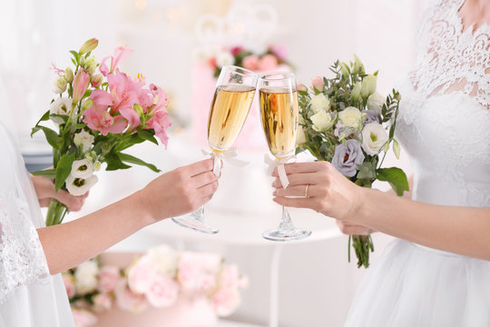 Young brides holding bouquets of beautiful flowers and glasses with champagne on lesbian wedding