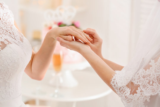 Young lesbian bride putting ring on finger of her future wife