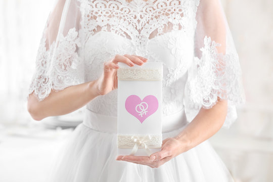 Young lesbian bride with invitation card on light background