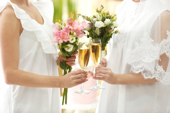 Young brides holding bouquets of beautiful flowers and glasses with champagne on lesbian wedding