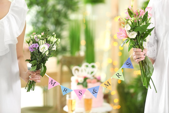 Happy brides holding bouquets of beautiful flowers and garland on lesbian wedding