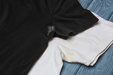 Black and white t-shirts with stains of sweat and deodorant on wooden background. Concept of hygiene - obrazy, fototapety, plakaty