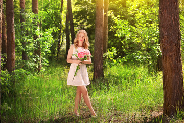 Beautiful young woman with bouquet of peonies in forest on sunny day