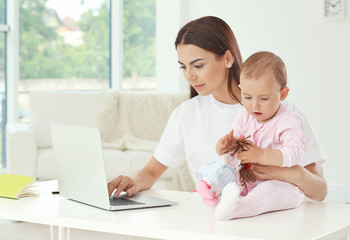 Young mother holding baby while working in home office