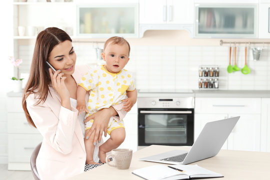 Young mother holding baby while working in home office
