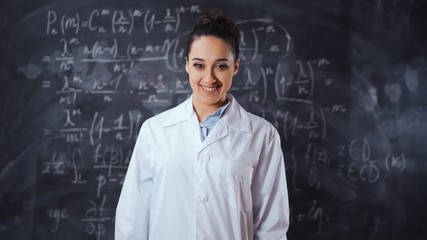 Young student female in white robe solve hard and heavy to understand math equation on black chalk board, She turn to camera and smile. Smart, clever, intelligent scientist woman concept. - Powered by Adobe