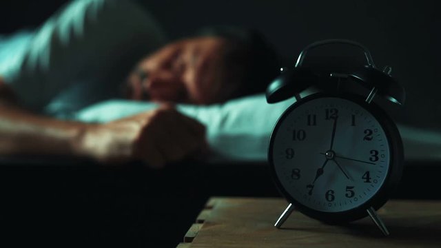 Restless man lying in his bed in morning, selective focus on bedside table with vintage alarm clock