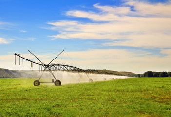 Modern agricultural  irrigation system watering a farm field on sunny summer day. Automated mobile irrigation sprinklers system with wheels on cultivated agricultural field.