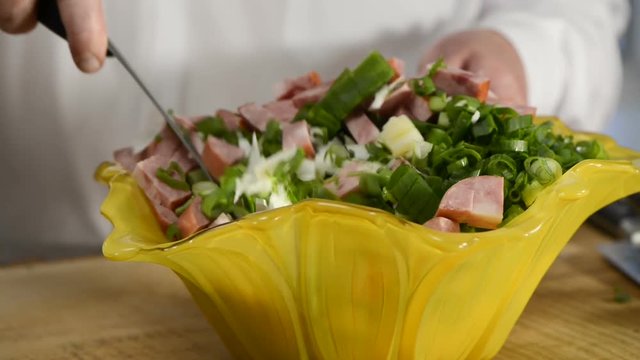 The cook mixes vegetables and ham salad in beautiful ware