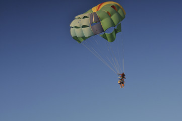 Люди летят на парашюте над морем на закате